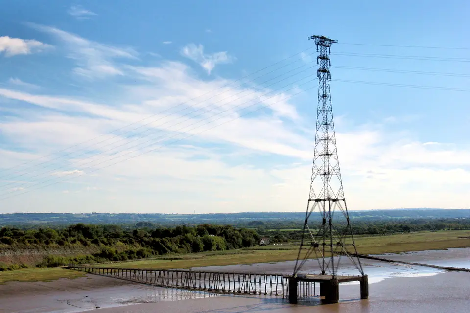 A tall steel lattice pylon on a concrete pier in the River Severn estuary, its cables running off across the water.