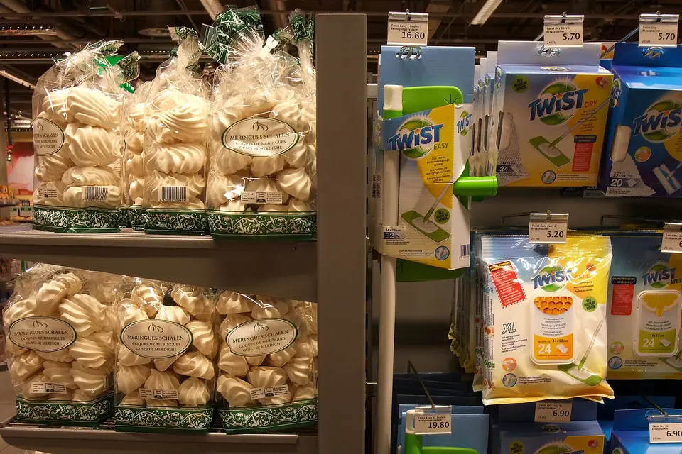 Bags of meringues on a supermarket shelf next to boxed cleaning mops with price tags.